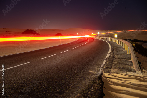 asphalt road running through the sandy desert at night