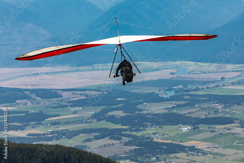 Fototapeta Naklejka Na Ścianę i Meble -  Hang gliding in action. Hang Glider pilot launching over the Kootenay valley mountains, Creston, British Columbia, Canada