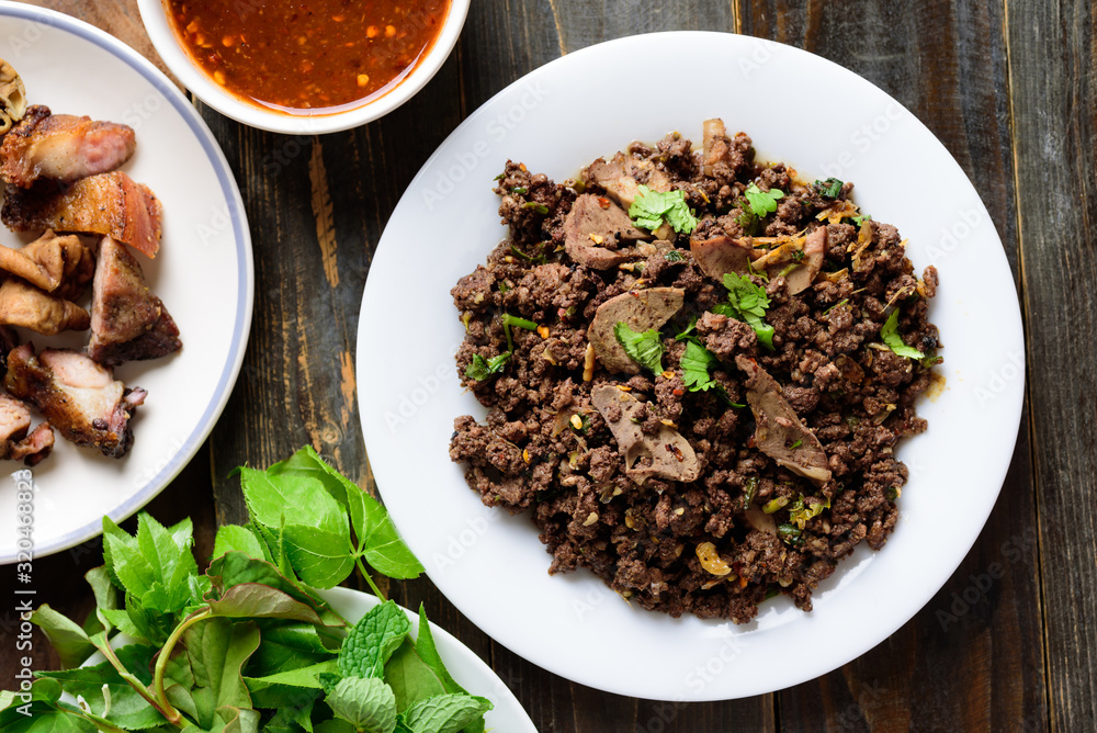 Northern Thai food, spicy minced pork salad (Larb Moo Kua) eating with grilled intestine and fresh vegetables on wooden background, top view Northern Thai food, spicy minced pork salad (Larb Moo Kua) eating with grilled intestine and fresh vegetables on wooden background, top view