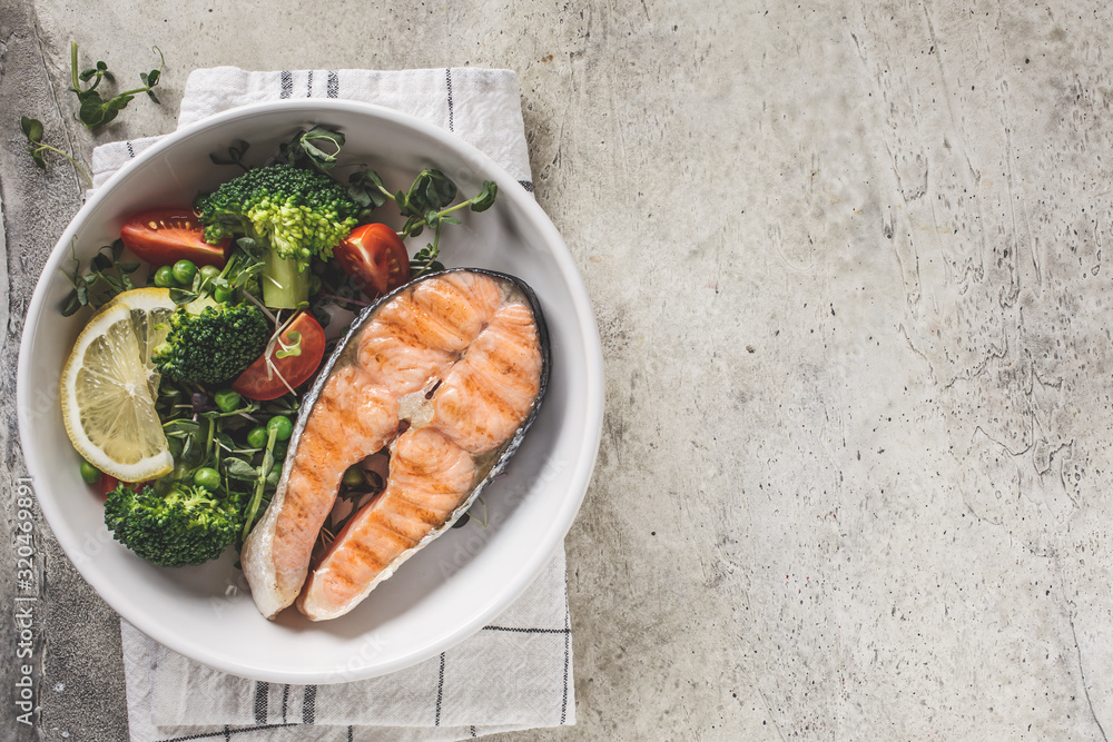 Grilled salmon steak with broccoli and tomatoes in a white plate on gray background, top view, copy space. Diet food concept. Grilled salmon steak with broccoli and tomatoes in a white plate on gray background, top view, copy space. Diet food concept.