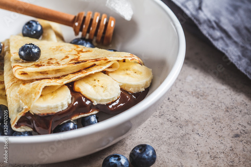 Crepes with chocolate, banana, berries and honey in a white plate. photo