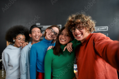 Enjoying time together. Positive group of multicultural people in casual wear making selfie on the phone while standing against blackboard in the creative office