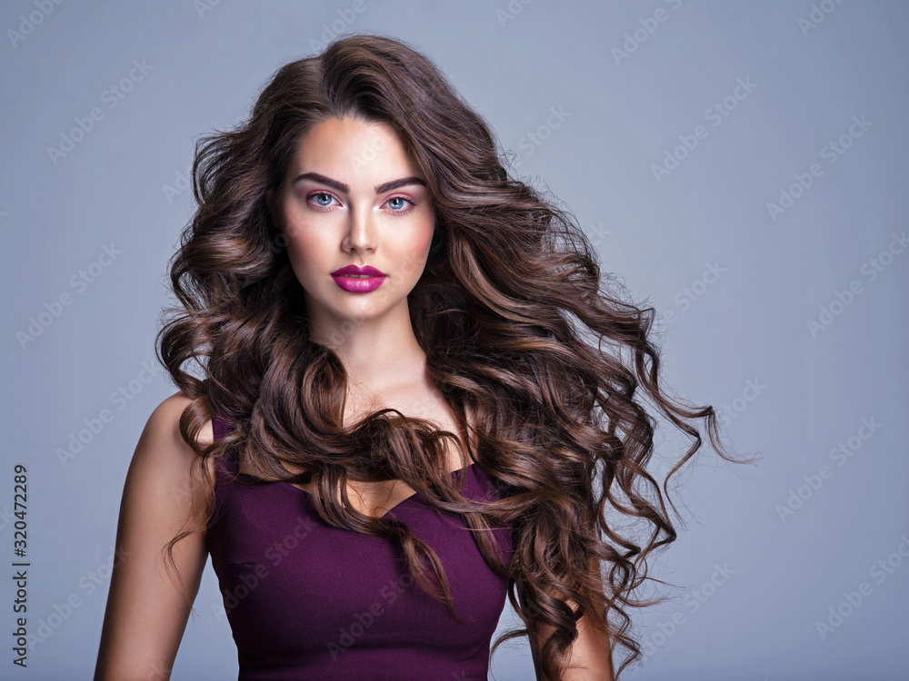 Face of a beautiful woman with long brown curly hair. Fashion model with  wavy hairstyle. Attractive young girl with curly hair posing at studio.  Female face with purple makeup. Violet make-up. Stock