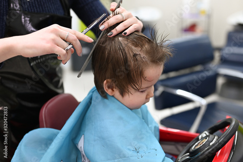 The child is getting a haircut at the hairdresser in a red car. The first haircut of the child in the hairdresser. Toddler child getting haircut.