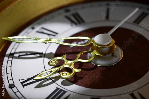 Vintage hands of an old golden clock casting a shadow on the dial with Roman numerals close up. Selective focus on hour hand