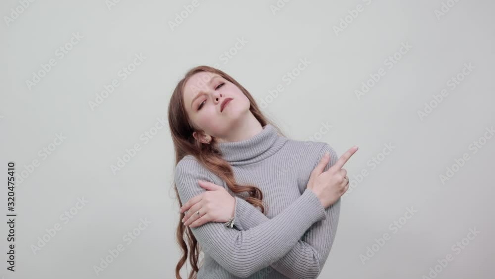 A young beautiful red haired woman in grey sweater poses stylishly and fashionably for the camera with her hands clasped A young beautiful red haired woman in grey sweater poses stylishly and fashionably for the camera with her hands clasped