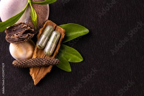 Herbal medicines concept. Ayurvedic capsules with green herbs, whole spices on black background and copy space photo