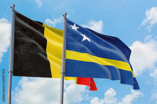 Curacao and Belgium flags waving in the wind against white cloudy blue sky together. Diplomacy concept, international relations.