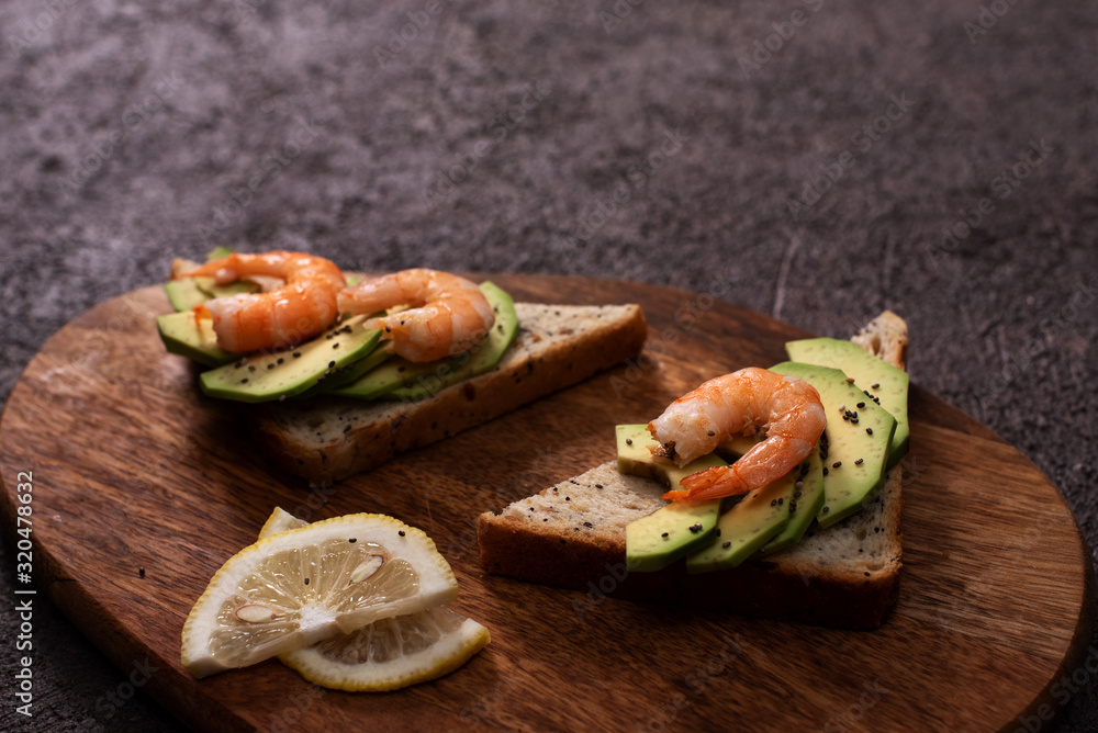 Wholegrain toast bread slices with guacamole, fried shrimp and fried bacon pieces on wooden board Selective Focus, Focus on the front of the shrimp on the first bread Wholegrain toast bread slices with guacamole, fried shrimp and fried bacon pieces on wooden board Selective Focus, Focus on the front of the shrimp on the first bread