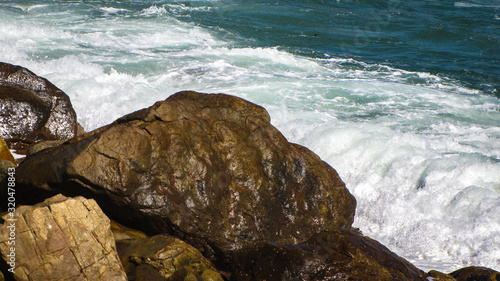 Sea waves splashing over wet rocky shore in capetown, South Africa