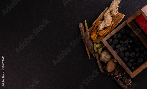 Foto Top view closeup of black ayurvedic tablets in a wooden box with assorted whole spices on a black background