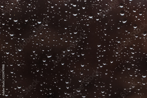 beautiful raindrops on glass window while raining with different texture with dark color blurred background.