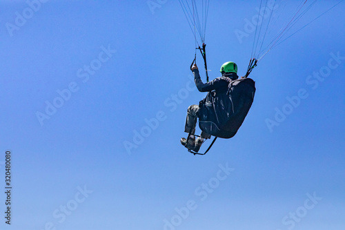 Flying paraglider against the blue sky. Extremal air sport lover having fun in the clear sky. View from the bottom. Copy space