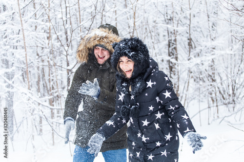 Love, relationship, season and friendship concept - man and woman having fun and playing with snow in winter forest