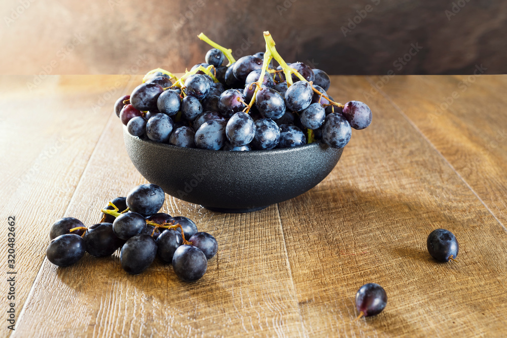 Bunch of black grapes in a bowl on wooden background. Bunch of black grapes in a bowl on wooden background.