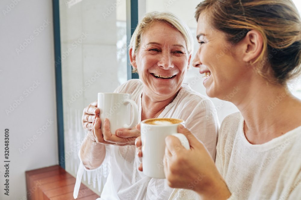 Laughing mature woman enjoying drinking coffee with her daughter and making plans for the day Laughing mature woman enjoying drinking coffee with her daughter and making plans for the day