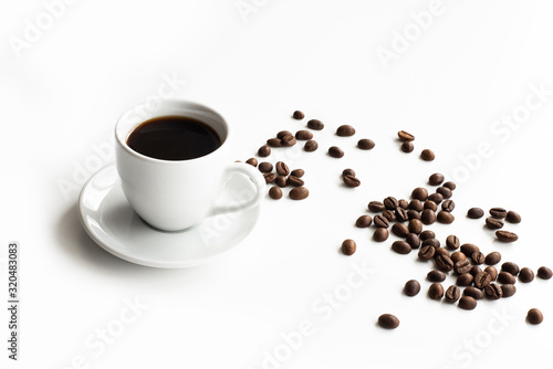 White cup of coffee and saucer on a white table scattered coffee grains with place for text top view