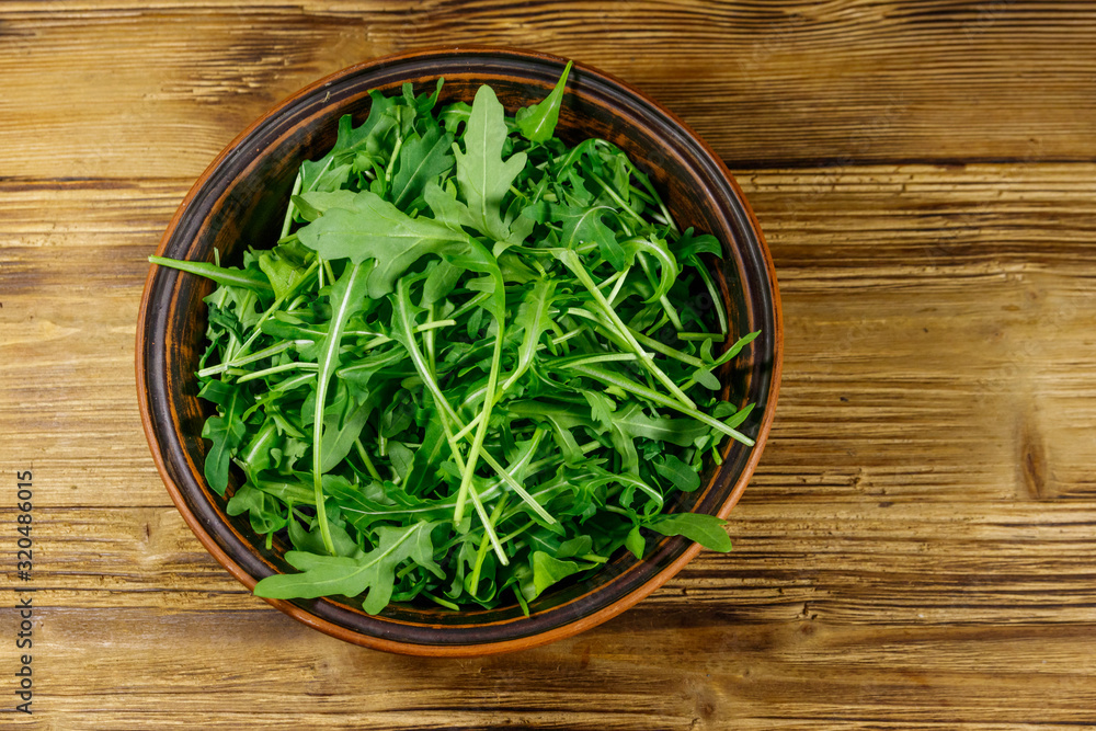 Fresh green arugula in ceramic bowl on a wooden table. Top view. Healthy food or vegetarian concept Fresh green arugula in ceramic bowl on a wooden table. Top view. Healthy food or vegetarian concept