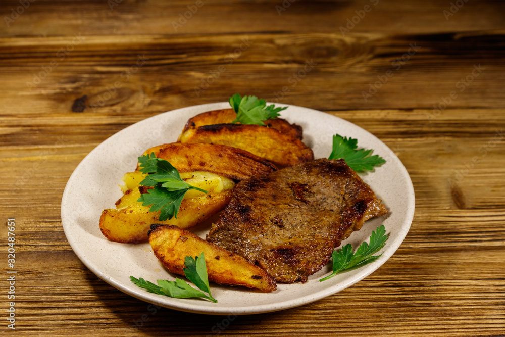 Fried beef steak with potato wedges on wooden table Fried beef steak with potato wedges on wooden table