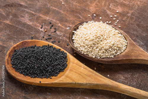 White and black sesame seeds in  spoons on wooden  background, top view, close up