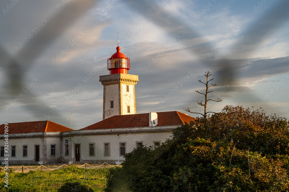 Alfanzina Lighthouse, shot through a chain link fence at dusk. The lighthouse is surrounded by fencing, near the town of Carvoeiro