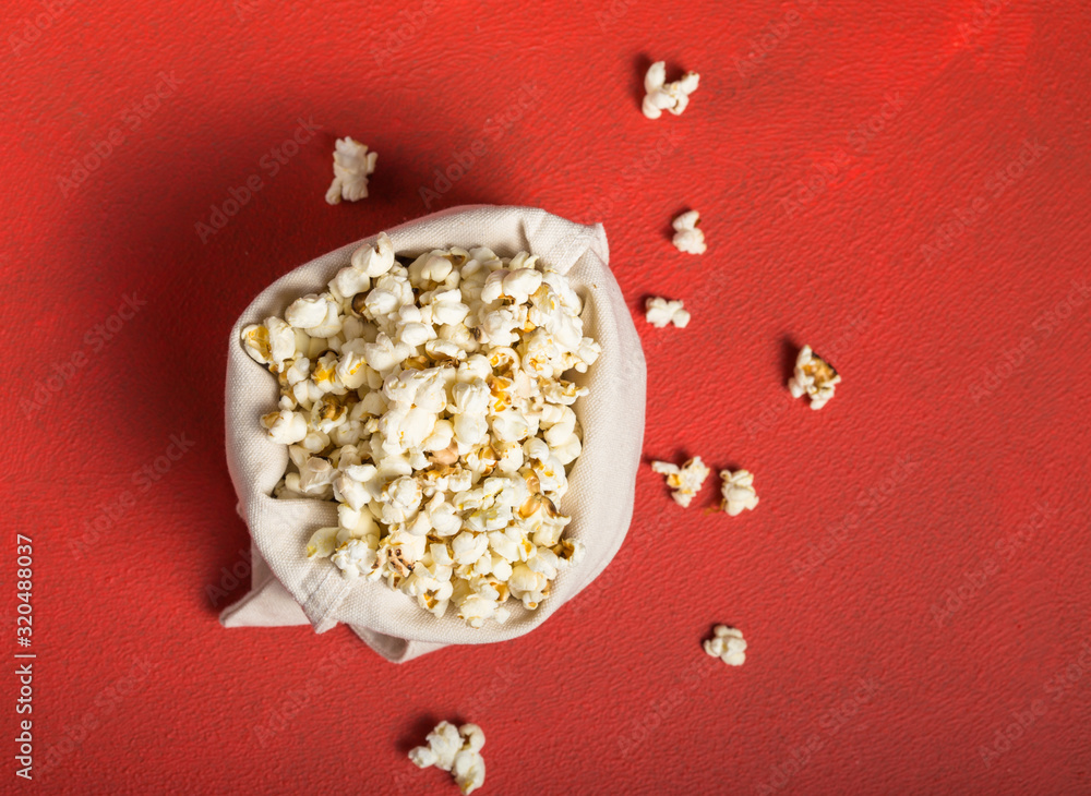 Fresh popcorn spilled out of the bag on a red background. Cinema snack concept. The food for watching a movie and entertainment. Copy space for text, flat lay. Fresh popcorn spilled out of the bag on a red background. Cinema snack concept. The food for watching a movie and entertainment. Copy space for text, flat lay.