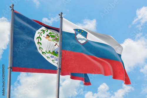 Slovenia and Belize flags waving in the wind against white cloudy blue sky together. Diplomacy concept, international relations.