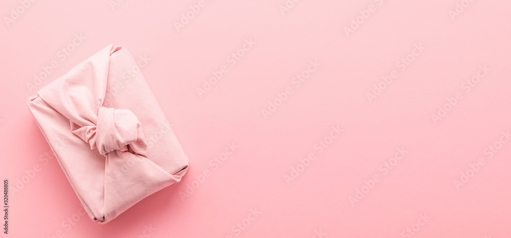 Holiday gift wrapped in cloth in the style of Furoshiki on a pink background. Zero Waste Life Holiday Concept. Holiday gift wrapped in cloth in the style of Furoshiki on a pink background. Zero Waste Life Holiday Concept.