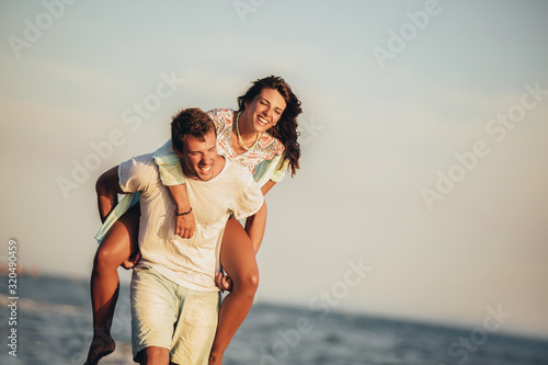Handsome young man giving piggyback ride to girlfriend on beach. Young couple enjoying summer holidays.
