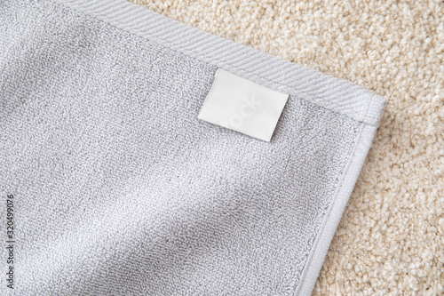 Grey terry towel with white empty label on beige pile carpet.