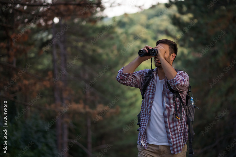 Happy adult man is hiking in forest. He is using binoculars.