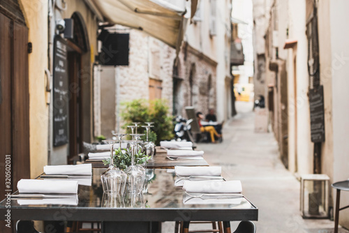 Fototapeta Naklejka Na Ścianę i Meble -  Outdoor restaurant in Italy. Empty glasses set in cafe with beautiful italian street at the background. Food, travel and  vacation concept