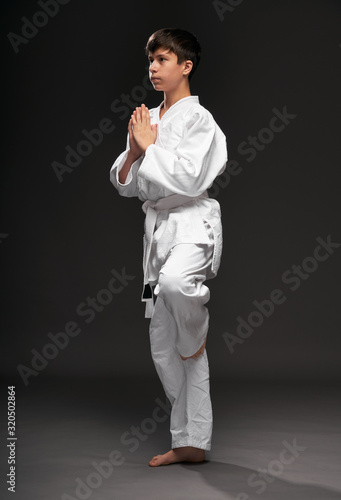 a teenager dressed in martial arts clothing poses on a dark gray background, a sports concept