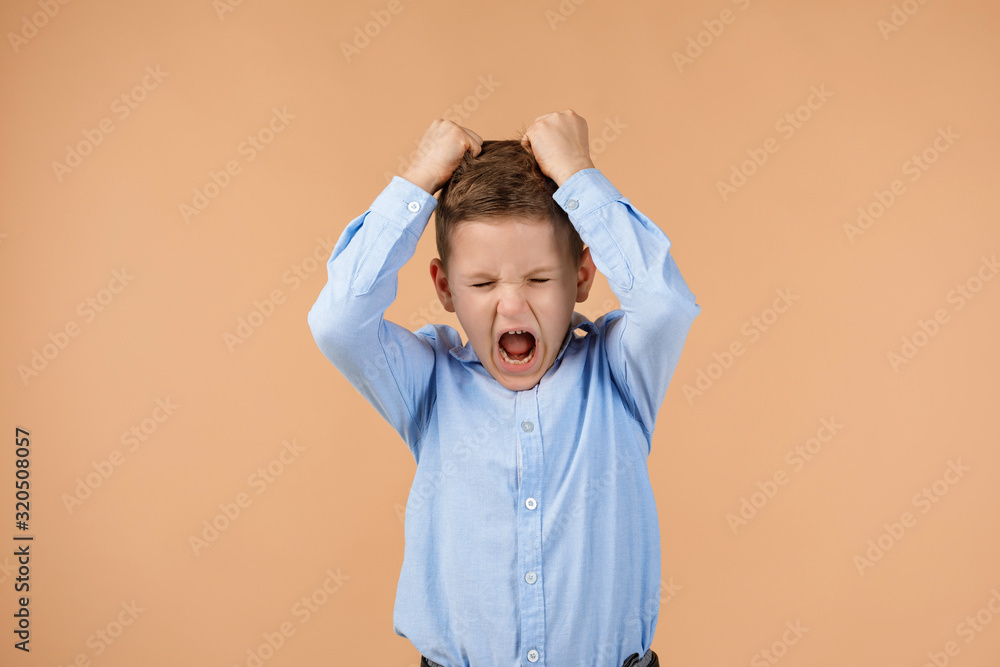 little child boy rips his hair and screams on beige background.