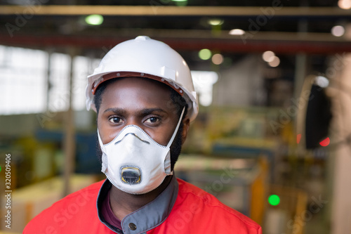 Portrait of Afro-American builder in respirator and hardhat standing at construction site photo