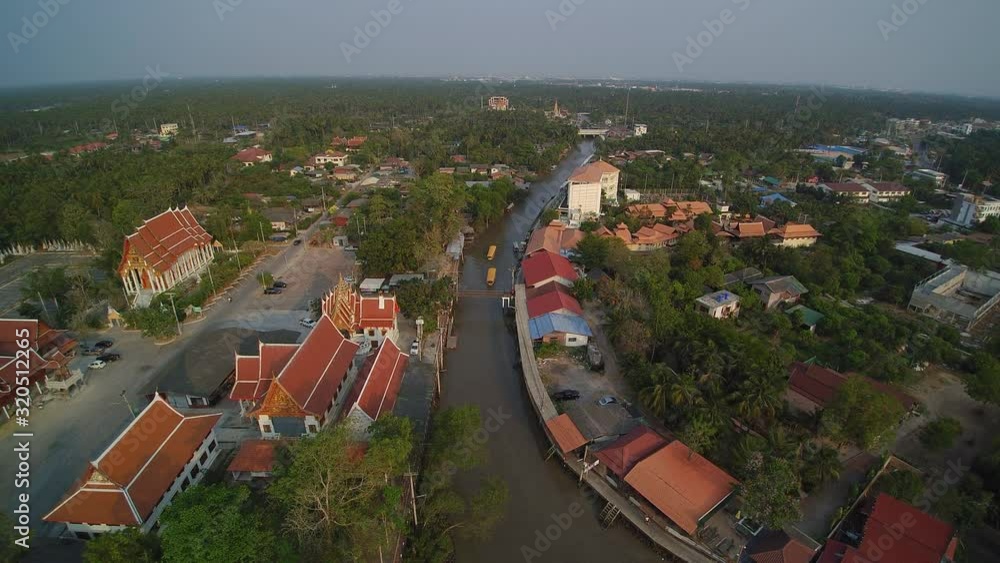 VDO. Aerial view of long-tail boats running in the canal around with old houses, buddhist temple, green trees and blue sky background, Amphawa Floating Market, Samut Songkhram, Thailand.