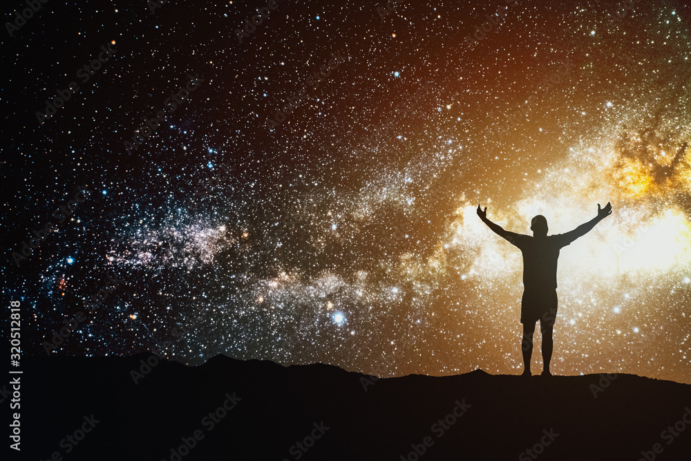 Night sky with stars cosmos and silhouette of a standing man with raised hands on the mountain. Landscape with Milky Way.
