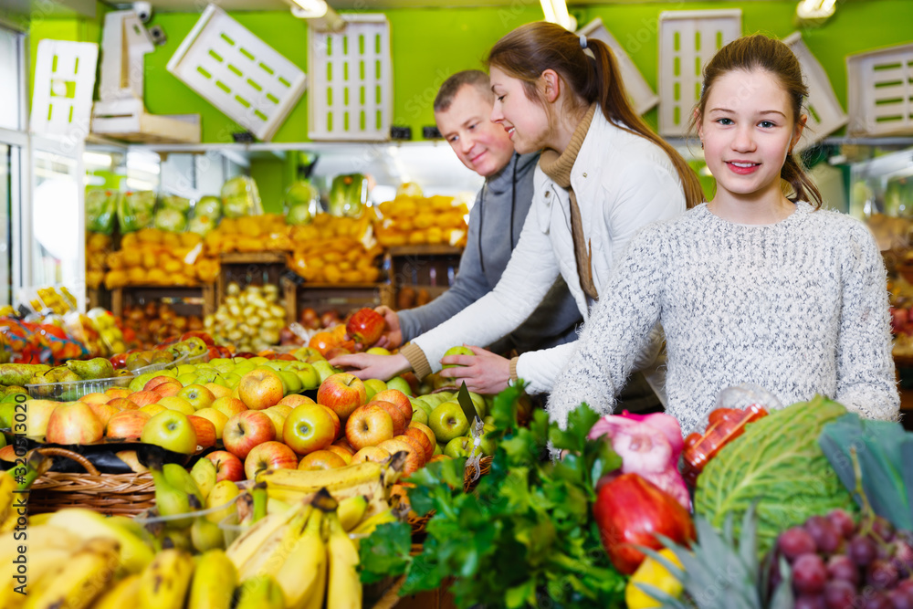 Preteen girl choosing ripe fruits and vegetables in greengrocery