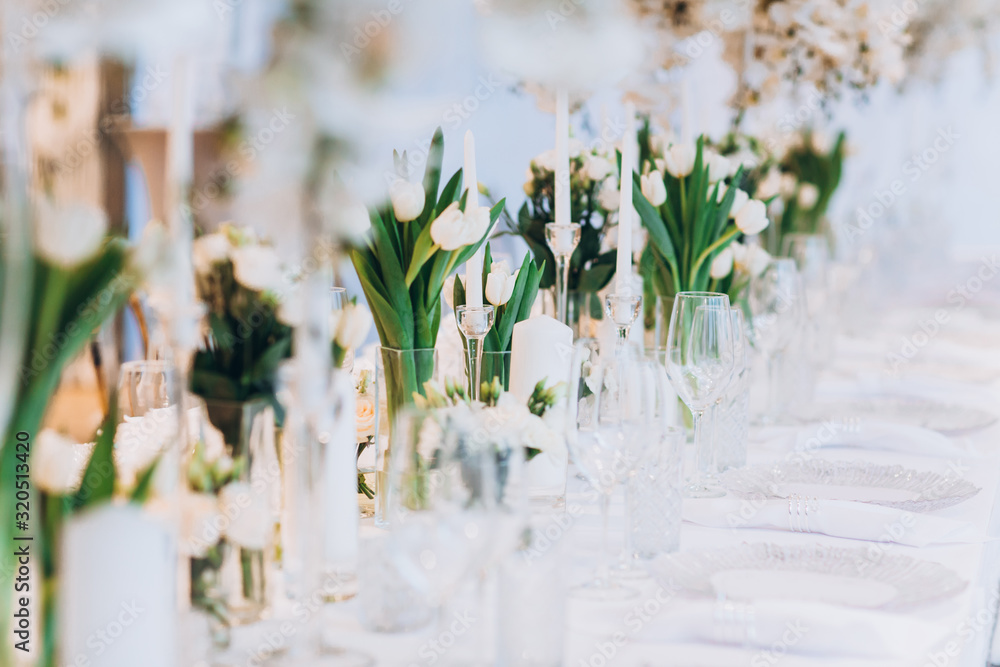 formal luxury elegant wedding decor restaurant tables served white tablecloth, plates, menus, glasses, tulips in vases, orchids, candles silver chairs, blue background - obrazy, fototapety, plakaty 