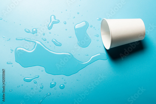 Tablou pe pânză Cup with spilled water on a blue background