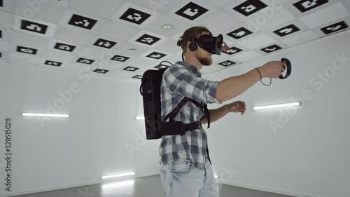 Young man in virtual reality headset is playing a videogame in an empty playroom full of white neon light, tracking arc shot, 360 degree photo