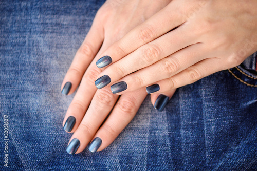 Hands with dark blue manicured nails on jeans textile background