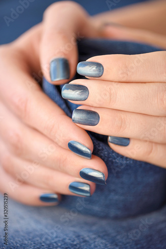 Hands with dark blue manicured nails on jeans textile background