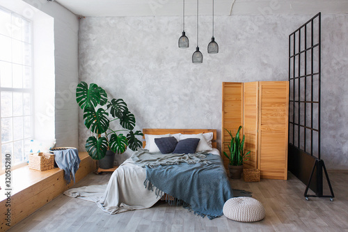 Cozy bedroom area at luxury studio apartment with a free layout in a loft style with big panoramic window and green plant. photo