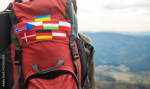 travel life style passion concept picture of backpack with country flags stripes of Ukraine, Germany, Austria, Denmark, Norway, Hungary and Czech Republic blurred background mountains highland view