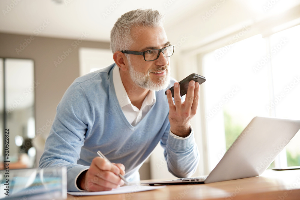 Man in office working on laptop computer and using smartphone