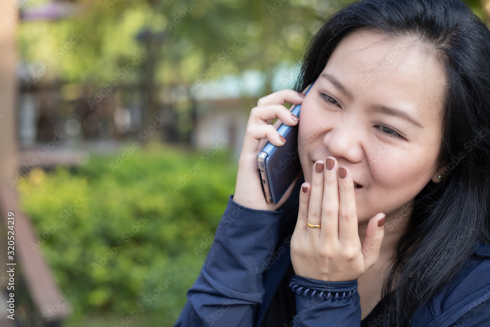 Asian woman talking on smart phone and holding her hand against her mouth at park. Communication concept. Extrovert characteristic. chit chat with friend. Asian woman talking on smart phone and holding her hand against her mouth at park. Communication concept. Extrovert characteristic. chit chat with friend.