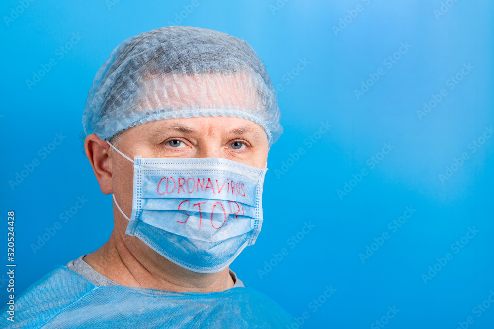 Portrait of ill man in medical unifrom and protective mask with stop coronavirus text at blue background. Respiratory protection. Coronavirus concept with copy space Portrait of ill man in medical unifrom and protective mask with stop coronavirus text at blue background. Respiratory protection. Coronavirus concept with copy space