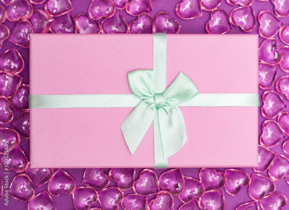 Flatlay with pink gift box with minty atlas ribbon on background from pink decorative hearts Flatlay with pink gift box with minty atlas ribbon on background from pink decorative hearts