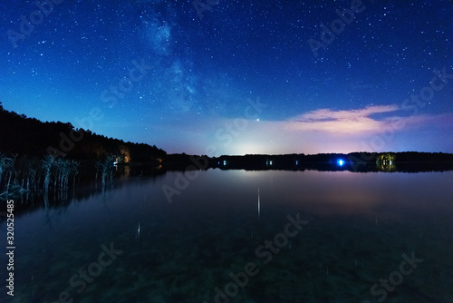 A magical starry night on the river bank with a large tree and a milky way in the sky and falling stars in the summer. 